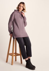Purple hoodie with drawstring and side slits, paired with black jeans and black ankle boots. Smooth fabric and relaxed fit.