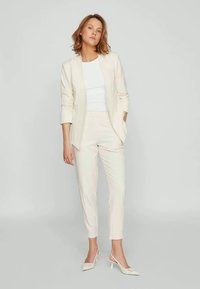 Completo chiaro con blazer aderente a un bottone e pantaloni affusolati, realizzato in un tessuto morbido e texturizzato. Abbinato a tacchi bianchi.