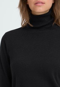 Schwarzer Rollkragenpullover aus weichem Stoff, mit geripptem Kragen und Bündchen. Glatte Textur mit tailliertem Design. Keine sichtbaren Muster.