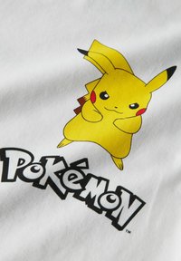 Biała tkanina z żółtym rysunkowym bohaterem z wysmukłymi uszami i czerwonymi policzkami, towarzyszącym napisem "Pokémon" napisanym grubą czarną czcionką.