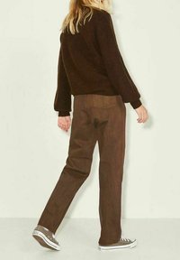 Braune Cordhose mit geradem Bein, die eine leicht lockere Passform zeigt und mit grauen Turnschuhen kombiniert wird. Das Oberteil besteht aus einem strukturierten, dunklen Stoff.