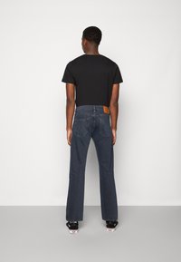 Svart t-shirt och mörkblå jeans med raka ben, med en läderpatch på bakre midjebandet och två bakfickor. Mjuk denimtextur.