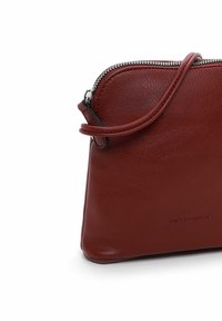 Bolso de hombro de cuero rojo con forma redondeada, cierre de cremallera y una sola correa. Presenta una marca mínima en una fuente sutil.