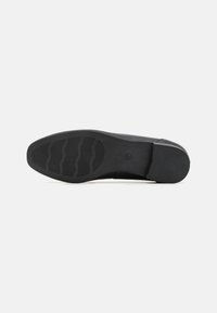 Semelle de chaussure noire en caoutchouc texturé pour une meilleure adhérence, avec un bout arrondi, des bords lisses et des rainures horizontales pour une traction accrue.