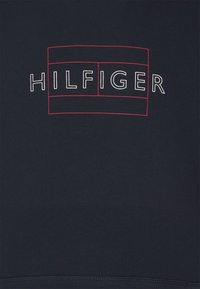 Sudadera naval de tela suave con un destacado logotipo blanco "HILFIGER" contorneado en rojo, ubicado dentro de un diseño rectangular.