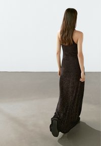 Lungo vestito nero con spalline sottili, tessuto testurizzato e silhouette aderente, che scorre fino al pavimento con una leggera scia.