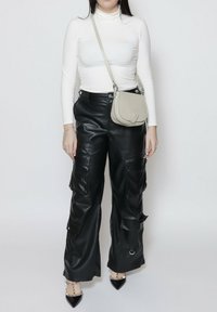 Pantaloni cargo neri in similpelle con molteplici tasche, abbinati a un dolcevita bianco e a una borsa a tracolla grigia chiara. Tacchi a spillo neri.
