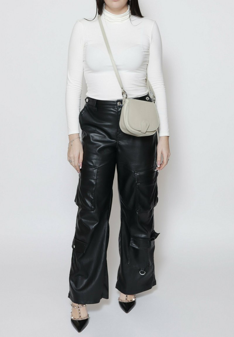 Pantaloni cargo neri in similpelle con molteplici tasche, abbinati a un dolcevita bianco e a una borsa a tracolla grigia chiara. Tacchi a spillo neri.