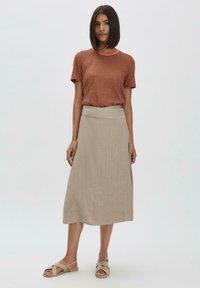 Braun gestreiftes Kurzarm-T-Shirt mit Rundhalsausschnitt, kombiniert mit einem beigen Leinenrock, der eine leichte A-Linie hat und einen dezenten Schlitz an der Seite.