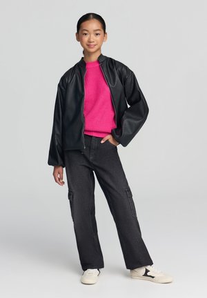 Giacca nera sintetica con zip, maglione rosa a maglia, pantaloni cargo scuri con tasche e sneakers beige. Outfit semplice e casual.