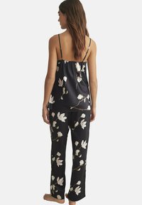 Ensemble de pyjama noir composé d'un haut sans manches et de pantalons longs avec un motif floral. Texture soyeuse avec des bretelles réglables et une coupe décontractée.