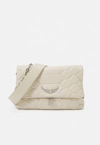 Gequilte beige tas met een zilveren, gevleugeld embleem, bovenste ritssluiting en een verstelbare riem. Heeft een opvallend patroon van diamantvormen.