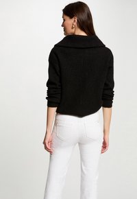 Black knitted sweater with a wide collar, textured fabric, and rolled sleeves, paired with light-colored jeans.