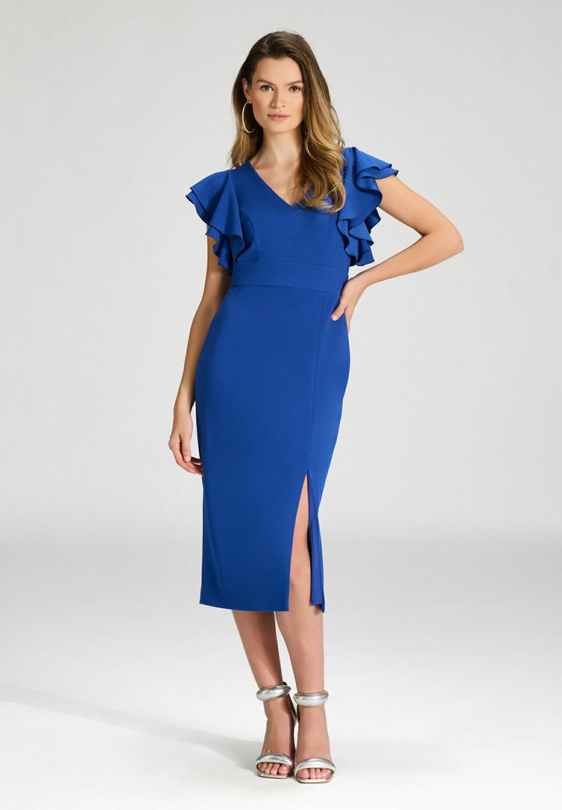 Robe moulante bleue avec des manches courtes à volants, un décolleté en V et une fente sur le côté, associée à des talons à lanières argentés. Matière lisse.