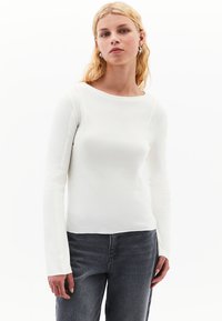 Vit långärmad topp med rund halsringning, slät yta och sömdetaljer, kombinerad med grå denimjeans. Enkel, minimalistisk design.