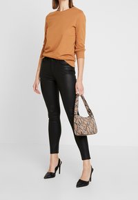 Bruin langemouwtrui, zwarte skinny broek en zwarte puntige hakken. Houdt een kleine handtas vast met een slangenleren patroon in bruin en zwart.