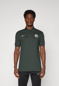 Mørkegrøn polo t-shirt med krave, korte ærmer, Nike-logo og Chelsea FC-badge på venstre bryst. Letvægts stoftekstur.