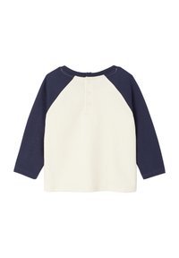 Langärmliges Shirt; Cremefarbener Körper mit marineblauen Raglanärmeln; Knopfverschluss auf der Rückseite; weicher Stoff mit glatter Textur; einfaches Design.