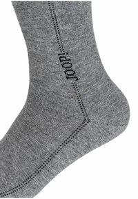 Calzino grigio realizzato in morbido tessuto texturizzato, caratterizzato da una cucitura diagonale e da un marchio nero sul lato. Design semplice con dettagli sottili.