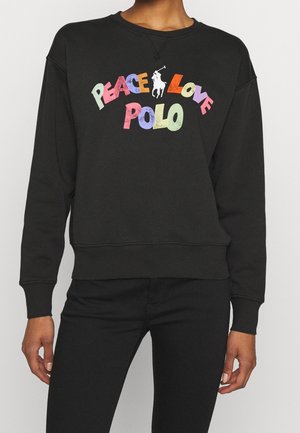 Personne portant un sweat-shirt noir avec le texte coloré « Peace Love Polo » et un logo de joueur de polo blanc centré sur la poitrine.
