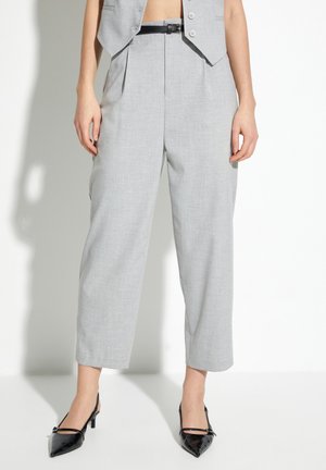 Pantalons tailleur gris clair à taille haute, avec plis et longueur raccourcie, associés à des escarpins noirs vernies à bout pointu.
