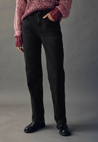 Schwarze Denim-Jeans im Straight-Leg-Schnitt mit sichtbaren Nähten, hoher Taille und zwei vorderen Taschen, kombiniert mit einem strukturierten roten Strickpullover.