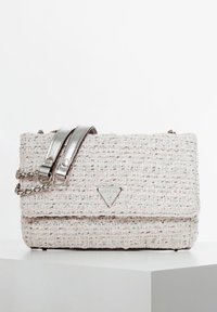 Teksturowana torebka w jasnoróżowym i kremowym kolorze z metalicznym srebrnym paskiem na ramię, zdobiona trójkątnym logo Guess na przodzie.