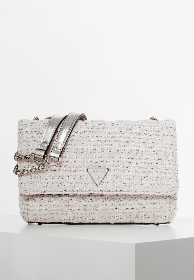 Teksturowana torebka w jasnoróżowym i kremowym kolorze z metalicznym srebrnym paskiem na ramię, zdobiona trójkątnym logo Guess na przodzie.