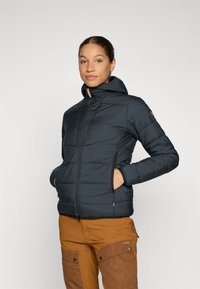 Doudoune bleu foncé avec capuche, fermeture éclair à l'avant, poches latérales et motif matelassé. Présente des accents beiges et une coupe ajustée.