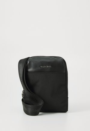 Borsa nera con una parte superiore in pelle liscia e un corpo in tessuto testurizzato. Presenta una lunga tracolla con dettagli del logo e una chiusura con zip. Forma compatta e rettangolare.