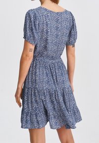 Niebieska sukienka w kwiatowy wzór z krótkimi bufiastymi rękawami, dopasowanym pasem i warstwową spódnicą. Wykonana z lekkiego materiału o miękkiej teksturze.