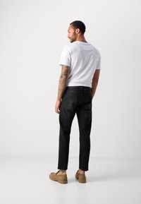 Jeans negri cu o croială dreaptă și două buzunare la spate, asortați cu un tricou alb simplu. Pantofii bej completează ținuta.