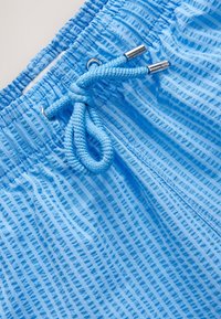 Ljusblå shorts med ett texturerat vertikalt randmönster, elastisk midjeband och en dragsko med metalliska ändar.