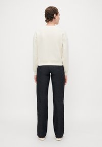Hvit cropped sweatshirt med drop skuldre, parret med mørk denim jeans med rett ben-design og baklommer.