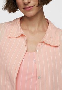 Camicia button-up rosa chiaro con strisce verticali bianche e un colletto leggermente sfrangiato. Presenta un piccolo "10" ricamato sul colletto.