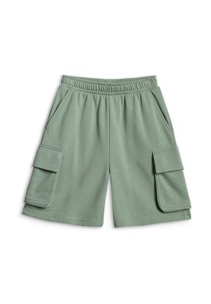 Garçon portant un t-shirt de volley-ball bleu clair, un short cargo vert, des chaussettes blanches, des baskets, tenant un sweat-shirt gris devant un fond gris uni.