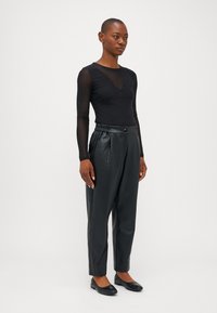 Haut noir à manches longues en matériau transparent avec des détails en perles, associé à un pantalon noir en simili cuir taille haute et des ballerines noires.