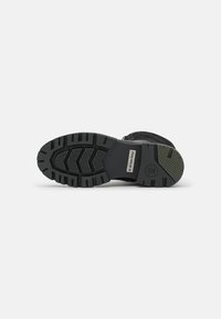 Suela de bota negra con goma texturizada, con surcos profundos para agarre y una placa de metal con el logo de la marca para mayor durabilidad.