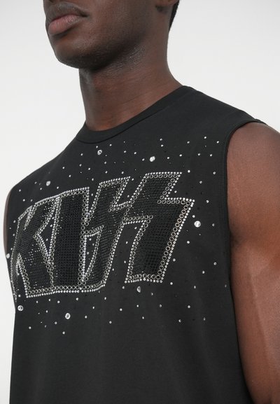 Fekete ujjatlan póló, amelyen a "KISS" szó strasszokból van kirakva, a textil más részein pedig szórtan szegecsek díszítik.