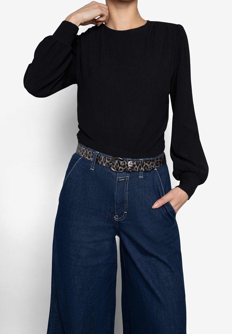 Femme portant un chemisier noir à manches longues rentré dans un jean taille haute bleu foncé à jambes larges avec une ceinture imprimé léopard.