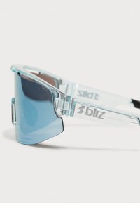 Lunettes de soleil transparentes bleues avec des verres larges et des branches épaisses, ornées de détails en métal argenté et d'un dégradé de teinte bleue.