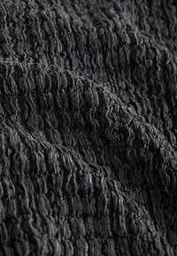 Tissu noir texturé avec des crêtes ondulées en relief créant un motif tridimensionnel sur une surface douce et flexible.