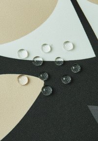 Tkano z geometrycznym wzorem w odcieniach beżu, czerni i bieli, z wyraźnymi i ciemnymi kroplami na powierzchni.