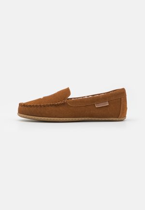Zapatilla mocasín de ante marrón con ribete cosido, suela blanda y forro interior acolchado, vista lateral sobre fondo blanco.
