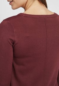 Maglione bordeaux a maniche lunghe con colletto a costine e trama lavorata. Presenta una cucitura verticale sul retro e maniche aderenti.