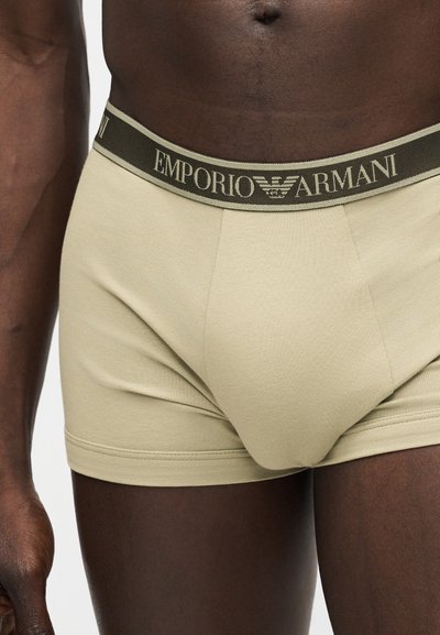 Ανδρικός κορμός που φοράει μπεζ μπόξερ Emporio Armani με ελαστική μέση με λογότυπο, ορατός από τη μέση έως το μέσο του μηρού.