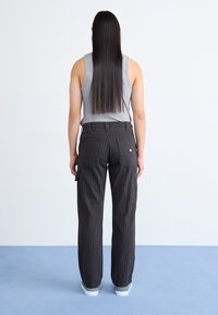 Pantaloni cargo negri cu dungi, cu două buzunare laterale, design cu picioare drepte și un elastic la talie. Un top gri fără mâneci este parțial vizibil.