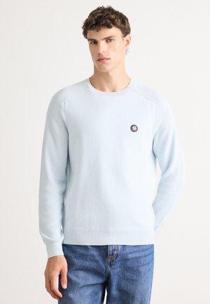Light blue sweater made of soft knit fabric, featuring a round neckline, long sleeves, and a small black circular logo on the chest.