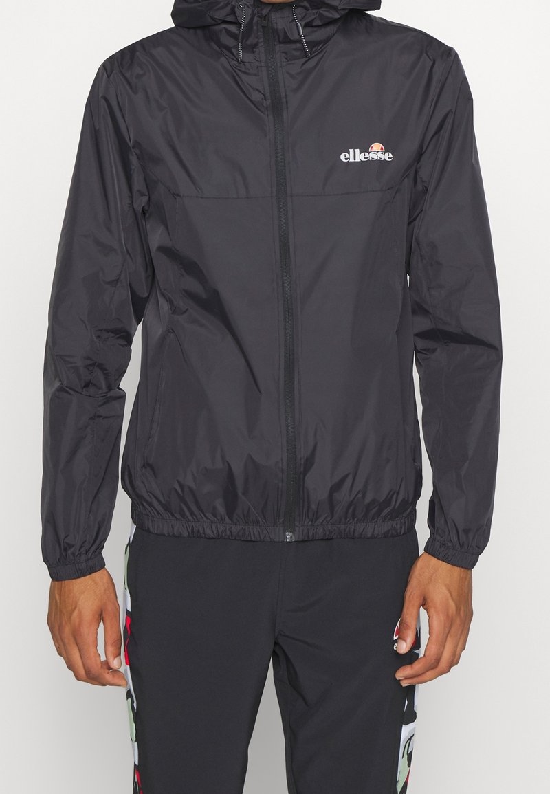 Coupe-vent léger noir avec fermeture éclair à l'avant, poignets et ourlet élastiques. Doté d'un petit logo blanc sur la poitrine et d'une capuche.