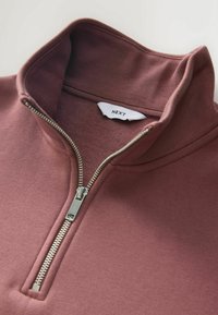 Bordowy pulower z połową zamka wykonany z miękkiego materiału. Posiada metalowy zamek błyskawiczny i prążkowany kołnierz. Widoczna metka jest biała z czarnym napisem "NEXT."